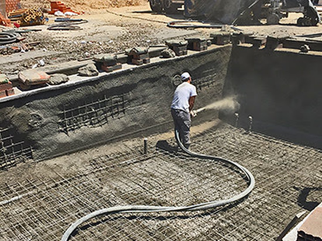 Operario proyectando hormigón (gunitado) sobre la ferralla de una piscina en obra